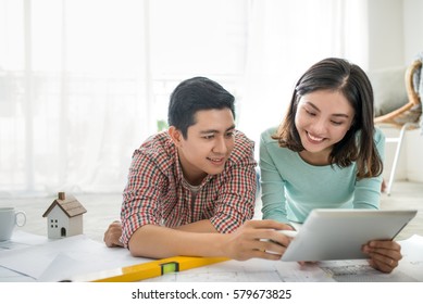 Attractive Young Asian Adult Couple Looking At House Plans.