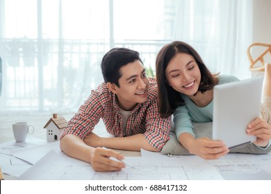 Attractive Young Asian Adult Couple Looking At House Plans.