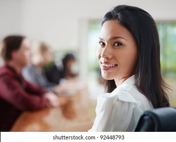 Attractive Young Asian Business Woman Smiling And Looking Over Shoulders At Business Meeting With Co-workers.