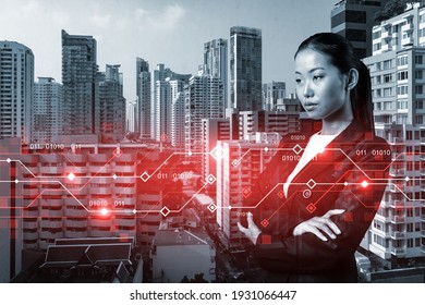 Attractive young Asian businesswoman pondering on technology at business process to achieve tremendous growth in commerce. Tech hologram icons over Bangkok background - Powered by Shutterstock