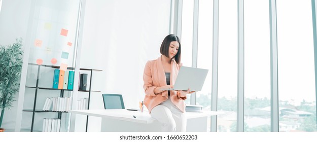 Attractive Young Asian Businesswoman Working On A Laptop At Table In Workstation Office, Thai Girl Enjoy Browsing For Online Shopping Store With Copy Space For Advertisement, For Banner Websites 