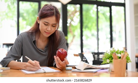 Attractive young asian female graphic designer eating an apple and sketching designing her design on paper at her office desk. - Powered by Shutterstock