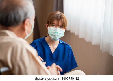 Attractive young Asian female nurse kneeling beside senior patient in wheelchair talking, smiling and cheering up in comfort at hospital. Healthcare and medicine concept.
