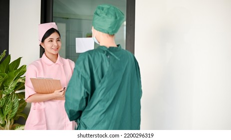 Attractive Young Asian Female Nurse Talking With A Female Surgeon In Front Of The Operating Room. Doctor, Physician, Surgeon Concept