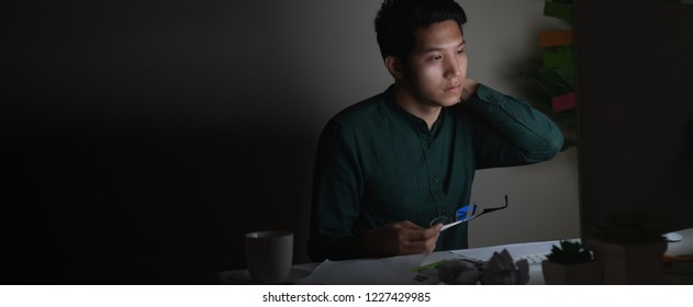 Attractive Young Asian Man Working Late At Night Looking At Laptop Computer In Dark Home Office Desk Feeling Tired On Work Load Or Work Hard Concept. Overworked Male Feeling Unhappy And Sleepless.