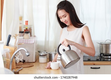 Attraktive junge asiatische schwangere Frau, die lockere Kleidung trägt, die sich in der Küche mit Schlamm posiert, und heiße Getränke gießt, die sich zuerst beleben. Gute schwangere Mutter, die in der Küche steht.