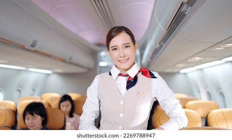 Atractiva joven azafata asiática con aspecto uniforme y sonriente a la cámara en avión, tripulación de cabina o concepto de ocupación de aeromozas