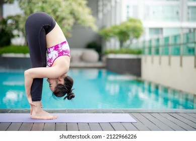 Attractive young Asian woman doing yoga exercise with uttanasana posing near swimming pool. Workout at home. Healthy lifestyle concept. International Yoga Day