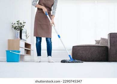 Attractive young Asian woman mopping tile floor at living room while doing cleaning at home during Staying at home using free time about their daily housekeeping routine. - Powered by Shutterstock