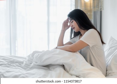 Attractive young Asian woman wake up on her bed looking unhappy and feeling sick.