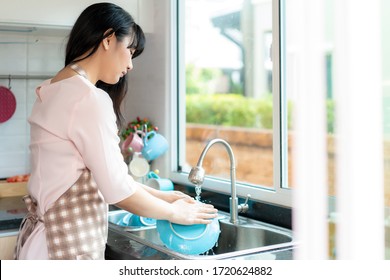 Attractive Young Asian Woman Is Washing Dishes At Kitchen Sink While Doing Cleaning At Home During Staying At Home Using Free Time About Their Daily Housekeeping Routine.
