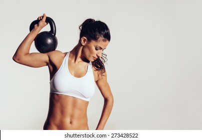 Attractive young athlete with muscular body exercising crossfit. Woman in sportswear doing crossfit workout with kettle bell on grey background.