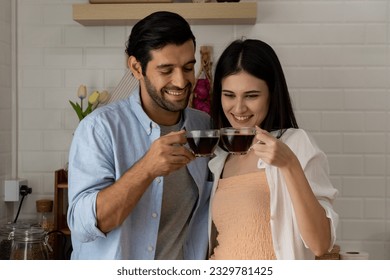 Attractive young beautiful woman and handsome man are happy spending time together while standing in modern kitchen with cup of coffee in hands. Romantic couple at home - Powered by Shutterstock
