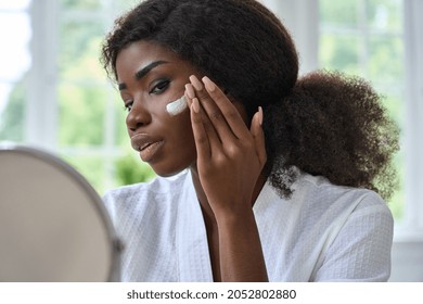 Attractive Young Black African Woman Model Touching Healthy Flawless Radiant Smooth Face Skin Care Looking In Bathroom Mirror Applying Facial Cream. Ethnic Beauty Skincare Morning Routine Concept