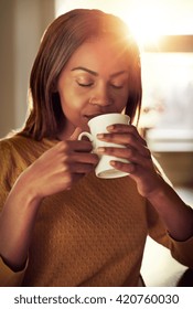 Attractive Young Black Woman Drinking A Cup Of Freshly Brewed Coffee Smelling The Aroma With Her Eyes Closed In Bliss As She Relaxes Indoors At Home