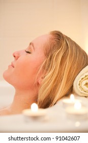 Attractive Young Blond Woman Lying In Bubble Bath With Candles (portrait)