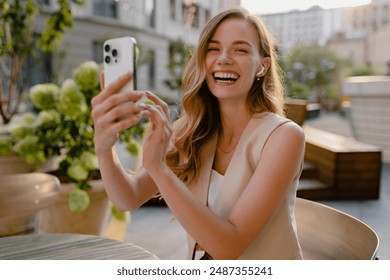 attractive young blond woman sitting in cafe using smart phone drinking coffee in spring summer autumn fashion trend outfit smiling happy in beige suit street style, laughing taking pictures on camera - Powered by Shutterstock