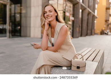 attractive young blond woman sitting in city street using smart phone in spring summer autumn fashion trend outfit smiling happy wearing beige suit and handbag style in sunny warm tones - Powered by Shutterstock