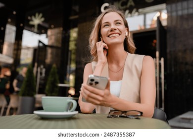 attractive young blond woman sitting in cafe using smart phone drinking coffee in spring summer autumn fashion trend outfit smiling happy wearing beige suit street style - Powered by Shutterstock