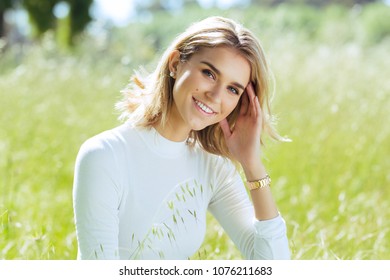 Attractive young blonde Caucasian woman in tight white top and denim posing outside in long grass - Powered by Shutterstock