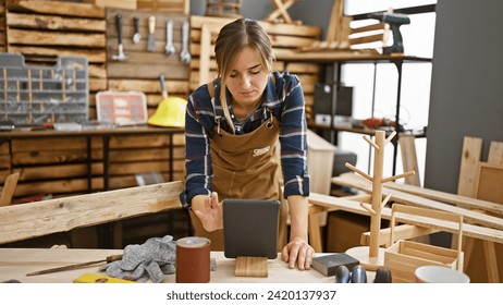 Attractive young blonde female carpenter immersed in her craft, proficiently using touchpad in bustling carpentry workshop - Powered by Shutterstock