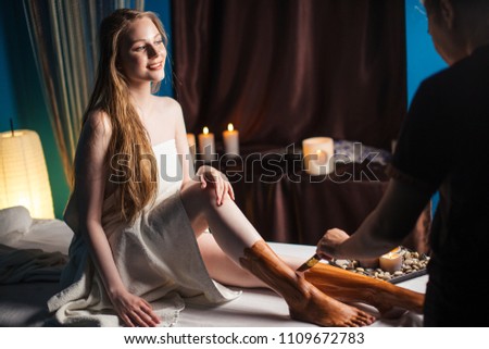 Attractive young blonde woman with long hair getting clay mask on feet after massage