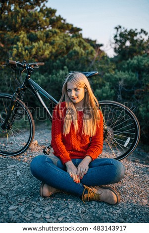 attractive young blonde woman in red sweater, blue jeans and yellow boots on the background of bike and forest and smiles
