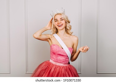 Attractive Young Blonde Woman Wearing A Crown, Pink Dress And A White Ribbon, Smiling. Beauty Contest Winner Concept.