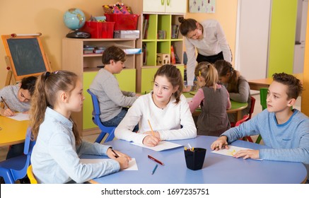 attractive young boy and girl holding thumbs up, standing in class with kids