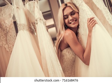 Attractive Young Bride Is Smiling While Choosing Wedding Dress In Modern Wedding Salon