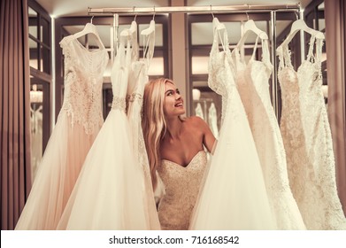 Attractive Young Bride Is Smiling While Choosing Wedding Dress In Modern Wedding Salon