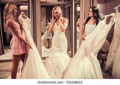 Attractive Young Bride Is Smiling While Choosing Wedding Dress In Modern Wedding Salon, Girls Are Showing More Dresses