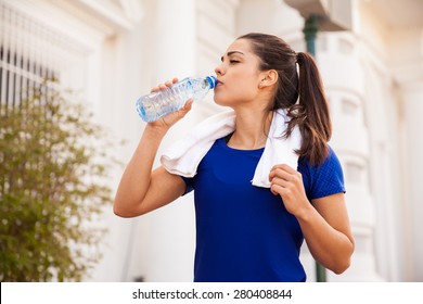 Attractive young brunette cooling down and drinking water from a bottle after working out in the city - Powered by Shutterstock