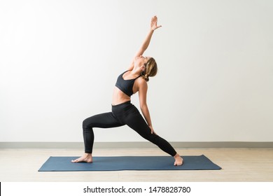 Attractive young brunette female in reverse warrior pose on exercise mat