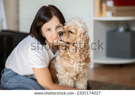 Attractive young brunette hugs her American cocker spaniel dog sitting at home on the floor. the concept of love for pets