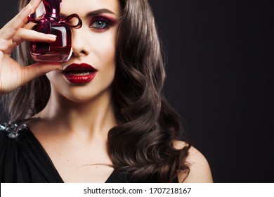 Attractive Young Brunette Woman And A Bottle With A New Fragrance, Use Perfume. Portrait On A Black Background