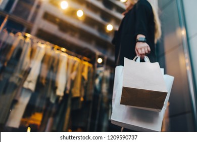 Attractive young business woman standing in front of shop window looking at smart clothing on a hanger, holding paper bags in hand and talking on mobile phone. Copy space for your text.