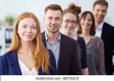 Attractive young businesswoman posing with her team of co-workers in a receding line behind her looking at the camera with a confident smile