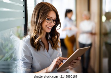 Attractive young businesswoman using a digital tablet while standing in front of windows in office - Shutterstock ID 2145880189