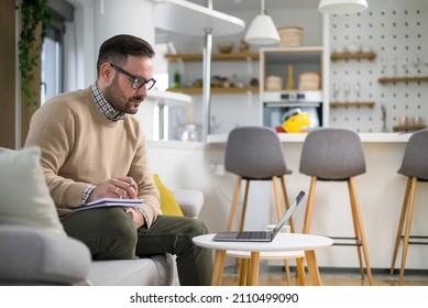 Attractive Young Caucasian Manager Working At Home Sitting In Sofa And Taking Notes. Concept Of New Way Of Living