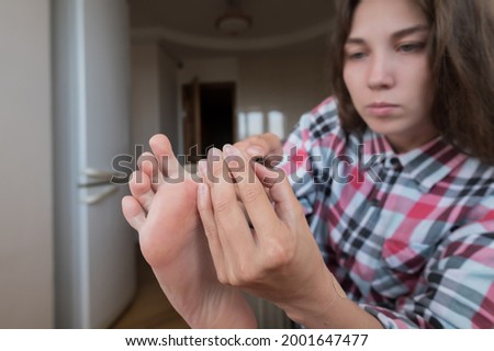 Attractive young Caucasian woman in a shirt sitting in the kitchen doing herself a pedicure. Indoor home care