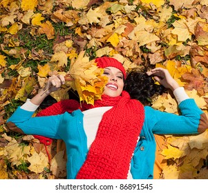 attractive young caucasian woman in warm colorful clothing lying down on yellow leaves outdoors smiling - Powered by Shutterstock