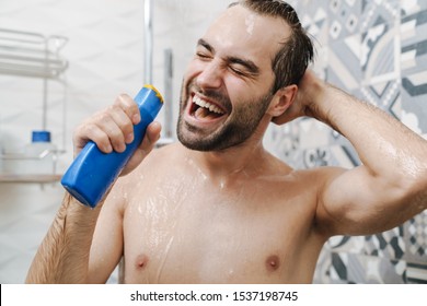 Attractive young cheerful man singing while washing in the shower, holding shampoo bottle - Powered by Shutterstock