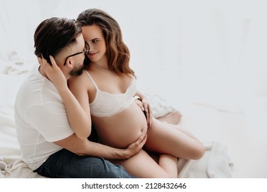 Attractive young couple expecting their baby, holding pregnant belly together and smiling