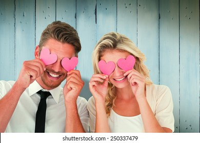 Attractive young couple holding pink hearts over eyes against wooden planks