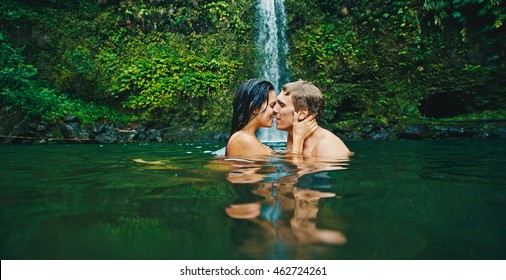 Attractive young couple kissing under jungle waterfall