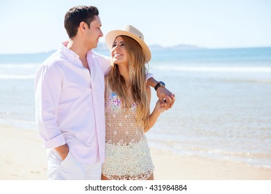 Attractive Young Couple Looking At Each Other Romantically During A Walk At The Beach