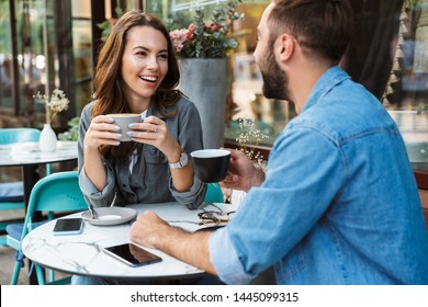 Attractive young couple in love having lunch while sitting at the cafe table outdoors, drinking coffee, talking