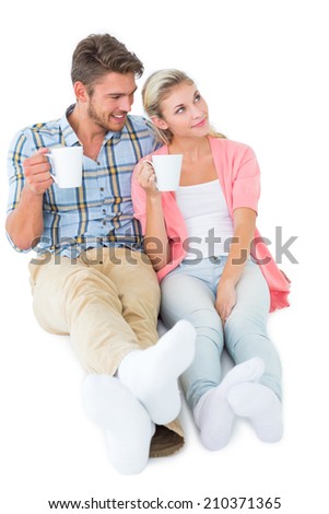 Attractive young couple sitting holding mugs on white background
