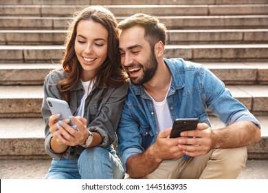 Attractive young couple sitting on stairs outdoors, looking at mobile phone - Powered by Shutterstock